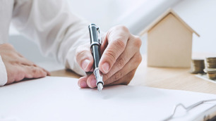 Imagem de uma mão assinando algo com uma caneta em um papel.