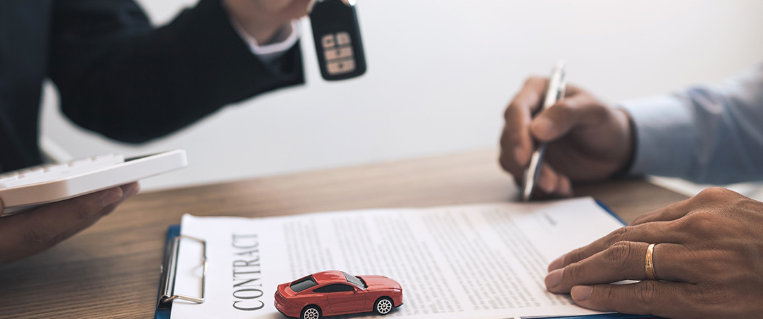 Homem assinando um contrato. Des focado há outro homem com uma chave na mão e em primeiro plano há um carro em miniatura..