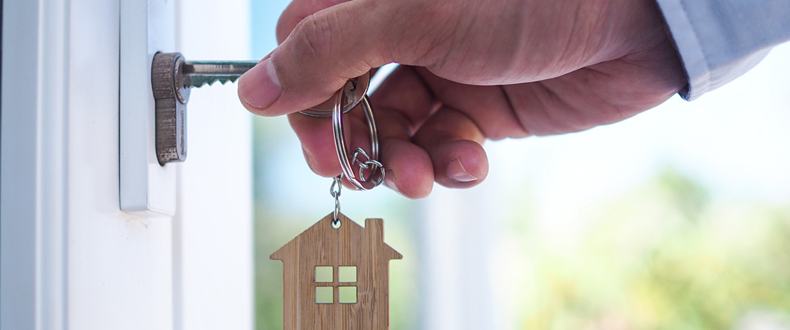 Homem colcoa chave na fechadura. No chaveiro há uma casa de miniatura.