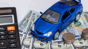 Ao lado uma calculadora, ao centro um carro azul em miniatura sobre várias notas de dólares e uma pilha de moedas ao lado.