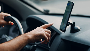 Mão quase encostando em um celular preso em um suporte no carro.