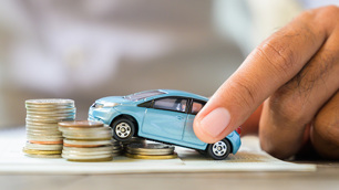 Mão empurrando um carro em miniatura em direção a uma escadinha de moedas.