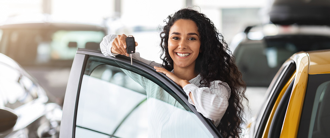 Mulher sorridente mostra a chave de um carro.