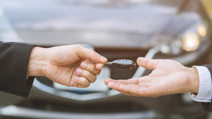 Mão entrega uma chave de carro para outra mão.