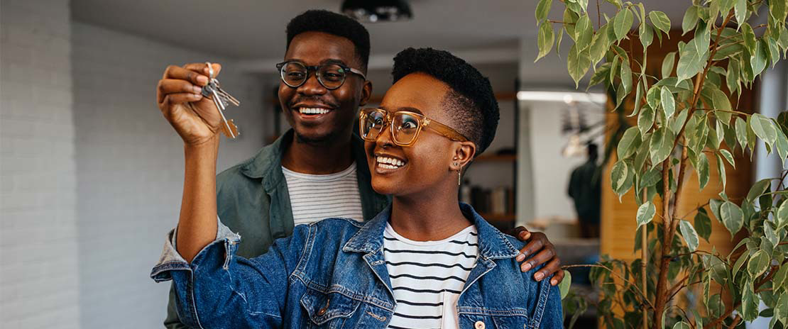Casal negro aparentando felicidade enquanto a mulher ergue uma chave de imóvel.