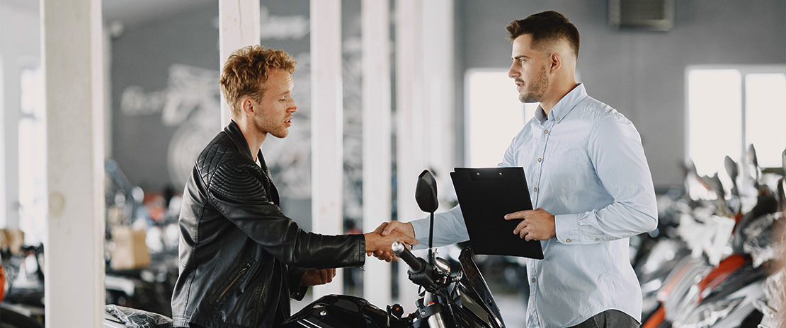 Dois homens apertando a mão e concluindo uma venda de uma moto.